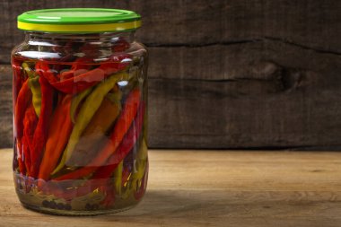 Kavanozda marine edilmiş acı biber, ahşap arka planda.