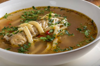 Erişteli tavuk çorbası ve beyaz kasede otlar.