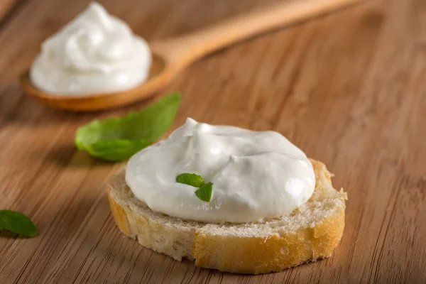Krem peynirli ve fesleğenli Fransız ekmeği ahşap arka planda.
