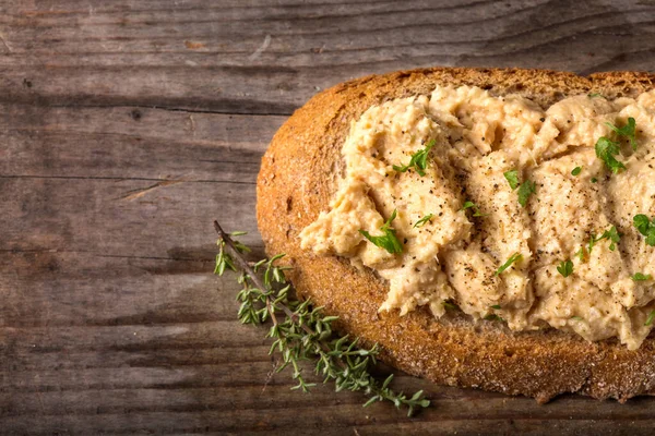 Kremalı ekmek dilimi. Püre tavuk göğsünden yapılmış. Otlar ve ahşap üzerine karabiber.