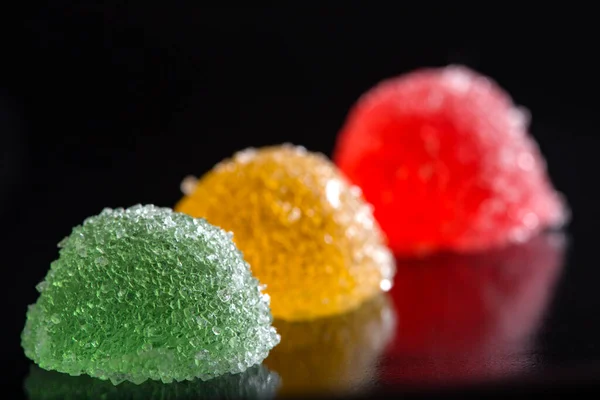 Koyu arkaplanda yansıması olan üç jöle şekeri.