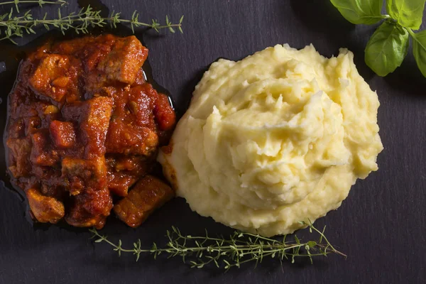 Domates soslu domuz yahnisi, patates püresi ve otlarla.