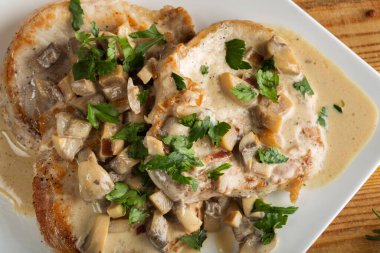 Beyaz soslu domuz filetosu ekşi krema ve maydanozlu mantarla ahşap zemin.