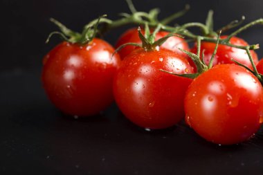 Koyu arkaplanda su damlaları olan bir avuç kiraz domatesi.