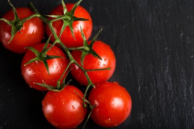 Koyu arkaplanda su damlaları olan bir avuç kiraz domatesi.