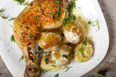 Bir kızarmış tavuk budu, yeni patates ve beyaz tabakta ekşi krema sosu.