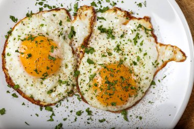 Beyaz tabakta iki kızarmış yumurta, tuzlu, karabiberli ve yeşil maydanozlu.