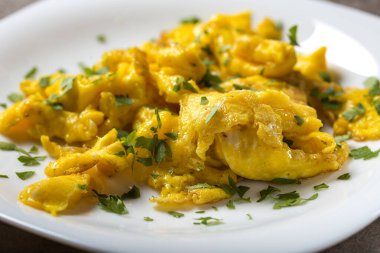 Yeşil maydanozlu, beyaz bir tabakta çırpılmış yumurta. Yakın görüş.