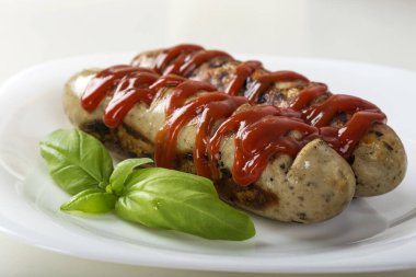 Sosisler ızgarada kızartılmış ve beyaz tabakta ketçap var. Yakın görüş.