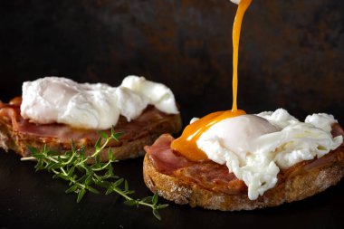 Koyu bir levhada ev yapımı Benedict yumurtalarının üzerine Hollandaise sosu döküyorum.