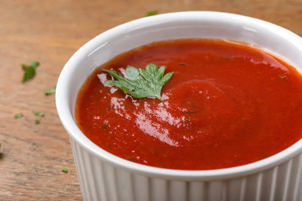 Beyaz kase ev yapımı domates sosuyla dolu, ahşap arka planda otlar var.