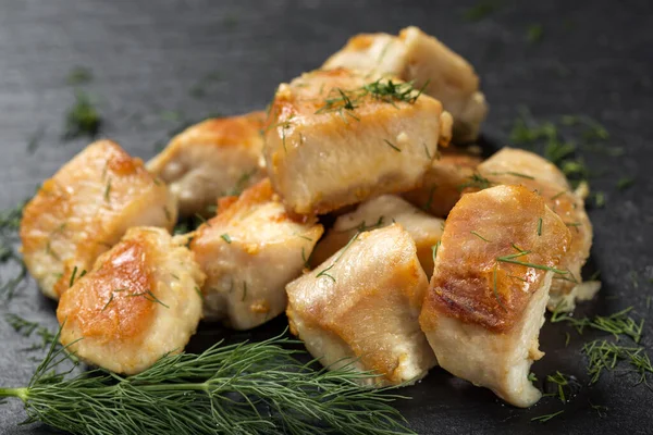 Koyu bir tahta üzerinde kızarmış tavuk göğsü parçaları. Yeşil dereotlu. Yakın çekim.