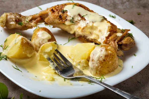 Bir kızarmış tavuk budu, yeni patates ve beyaz tabakta ekşi krema sosu.