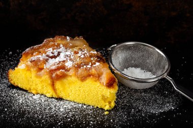 Koyu arkaplanda pudra şekerli bir dilim elmalı pasta.