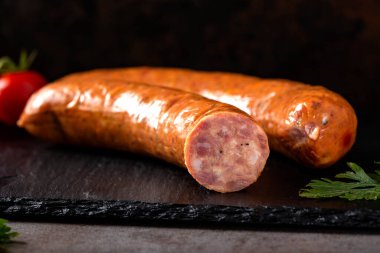 İki füme domuz sosisi, otlar ve koyu renkli domatesler.