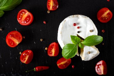 Fesleğenli Camembert peyniri koyu bir levhada dört renk biber ve kırmızı biber bırakır.
