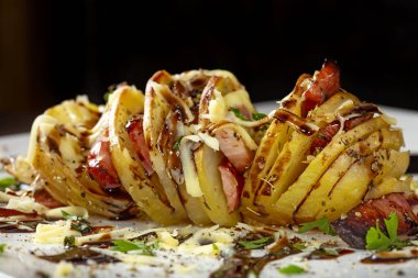 Domuz pastırması, sosis ve kremalı peynirli akordiyon patatesleri. Yakın plan.