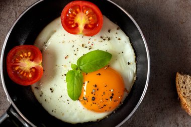 Küçük tavada bir yumurta, kiraz domatesli ve ekmekli.