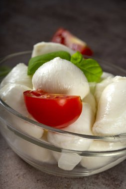 Mozzarella peynirli toplar, vişneli domates ve fesleğenli cam kase. Yakın görüş.