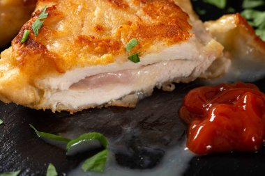 Koyu yeşil maydanozlu siyah bir tahta üzerinde bir parça Cordon bleu. Yakın çekim.