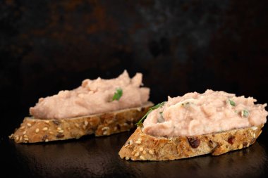 İki dilim ekmek, siyah bir levhada sebze ezmesi.