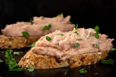 Sebze ezmeli iki dilim ekmek ve koyu bir levhada doğranmış yeşil maydanoz.