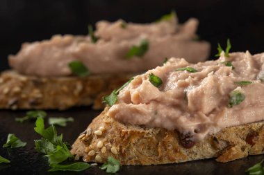 Sebze ezmeli iki dilim ekmek ve koyu bir tahta üzerinde doğranmış yeşil maydanoz. Yakın plan.