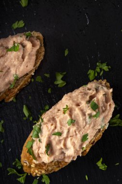 Sebze ezmeli iki dilim ekmek ve koyu bir tahta üzerinde doğranmış yeşil maydanoz.