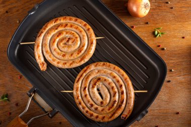 Baharatlı bir tavada iki ızgara domuz sosisi.