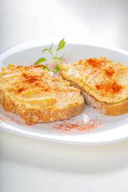 İki açık sandviç, humus ve beyaz tabakta kırmızı biber tozu. 