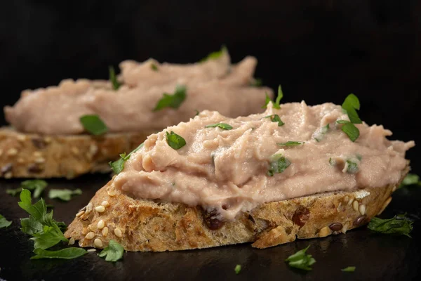 Sebze ezmeli iki dilim ekmek ve koyu bir levhada doğranmış yeşil maydanoz.