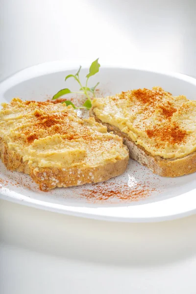 İki açık sandviç, humus ve beyaz tabakta kırmızı biber tozu. 