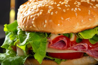 Tabakta salamlı, peynirli, domatesli ve soslu bir sandviç.