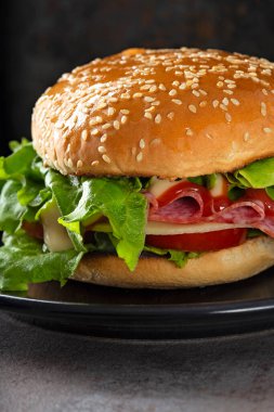 One sandwich with salami, cheese, tomatoes and sauces on the plate - vertical view