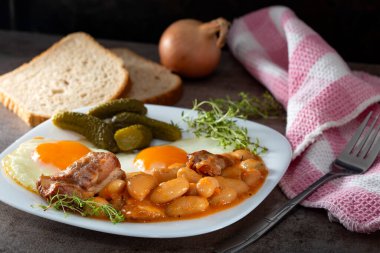 Füme domuz etli fasulye, yumurta ve turşu tabakta.