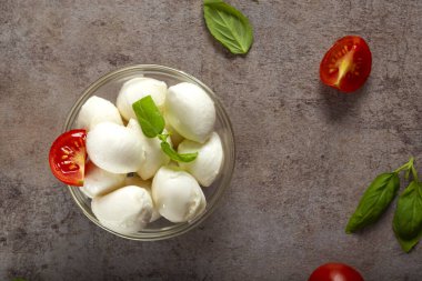 Çeri domatesli ve fesleğenli cam kasede küçük mozzarella topları.