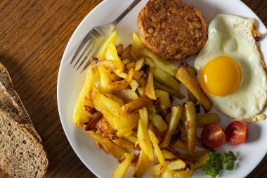 Kızarmış yumurtalı patates ve tabakta büyük bir köfte.