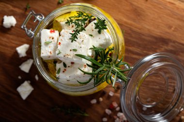 Zeytinyağında marine edilmiş Feta peyniri ve cam kavanozda taze bitkiler. Üst görünüm