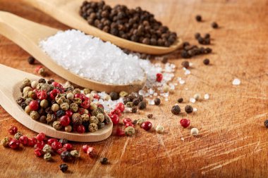 Ahşap arka plandaki ahşap kaşıklarda renkli biber ve deniz tuzu.