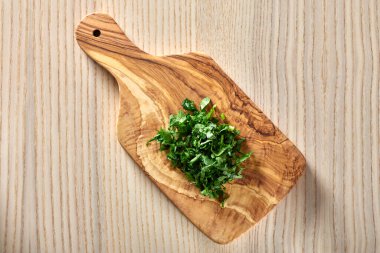 Zeytin ağacından yapılmış bir kesme tahtasının üzerinde doğranmış yeşil maydanoz.