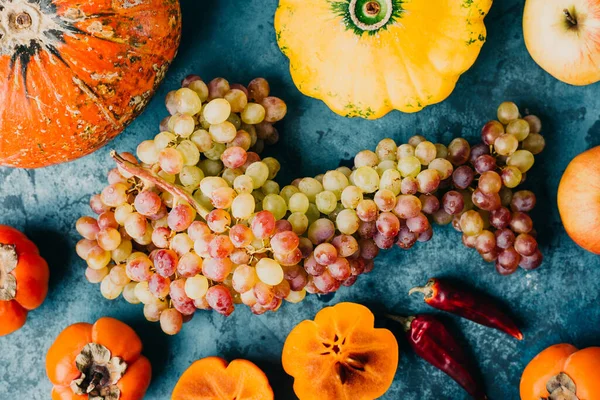 Herbstliches Obst und Gemüse. Trauben, Kürbis und Kaki auf blauem Hintergrund. — Stockfoto