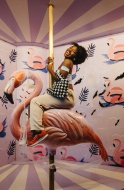 Gülümseyen siyah kadın pembe flamingo sürüşünde canlı Cadılar Bayramı temalı alanda