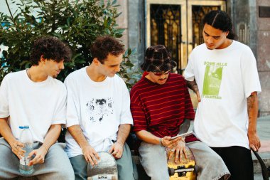 Şehirde dinlenen ve telefonu kontrol eden dört genç patencinin dikey portresi.