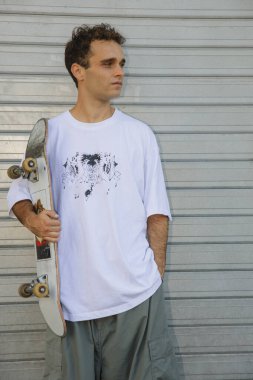 Şık, genç bir patenci kaykayını metal bir deklanşöre karşı tutarak duruyor..