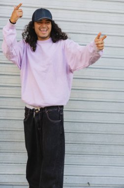 Sıradan giysiler içinde gülümseyen genç patenci dışarıda anlamlı el hareketleri yapıyor.