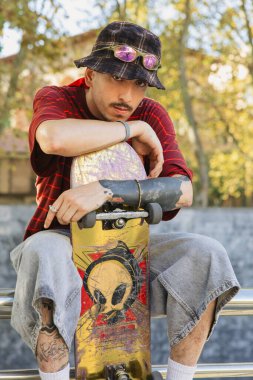 Kova şapkalı ve güneş gözlüklü havalı patenci şehirdeki kaykaylara yaslanıyor.