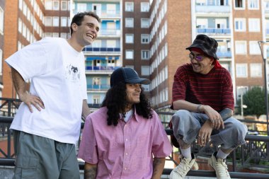 Üç genç kaykaycı şehir meydanında birlikte rahatlar ve gülümserler.