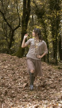 Botlu ve elbiseli genç bir kadın huzurlu bir sonbahar ormanında yürüyor.