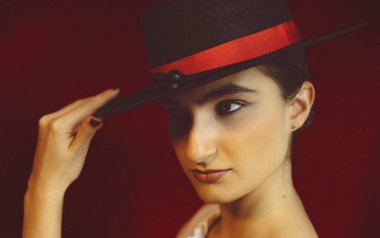 Siyah şapkalı beyaz kız, yoğun görünüşlü, kırmızı stüdyo arka planlı.