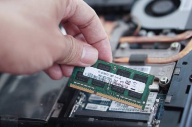 Bilgisayarın bellek modülünü açık dizüstü bilgisayarın şasisi üzerinde tutan bir elin yakın çekimi, kurulum veya yenileme için hazırlanma.